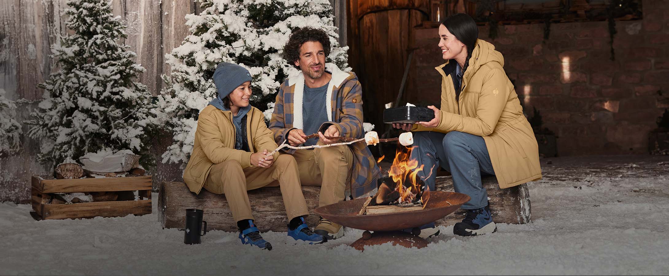 Vrouw, man en jongen dragen kleding uit de e.s.iconic-collectie in winterse omgeving rond een kampvuur