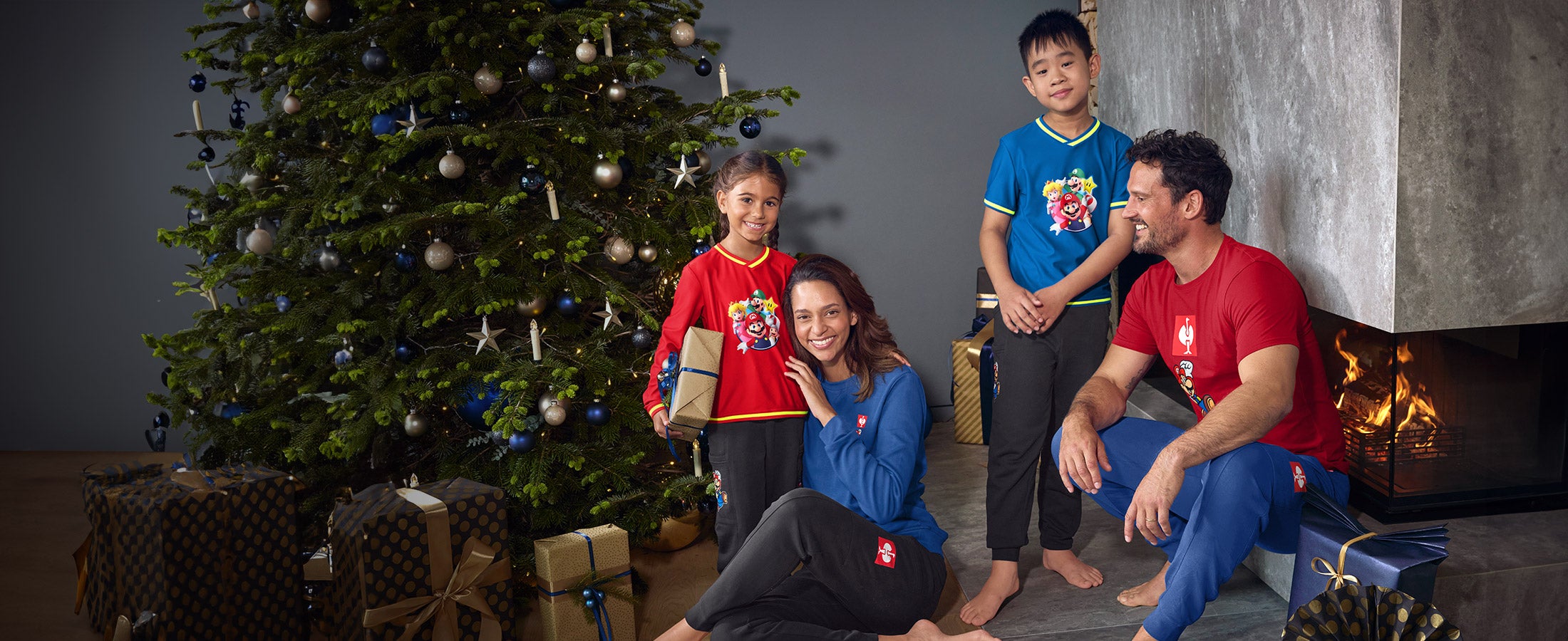 Vrouw, man, meisje en jongen dragen kleding uit de Super Mario x Strauss-collectie in woonkamer in kerstsfeer