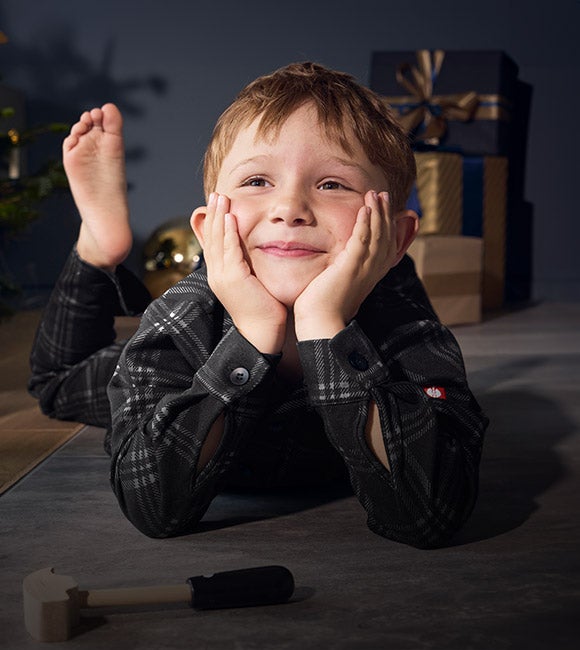 Een jongen draagt de e.s. ruitjespyjama in woonkamer in kerstsfeer