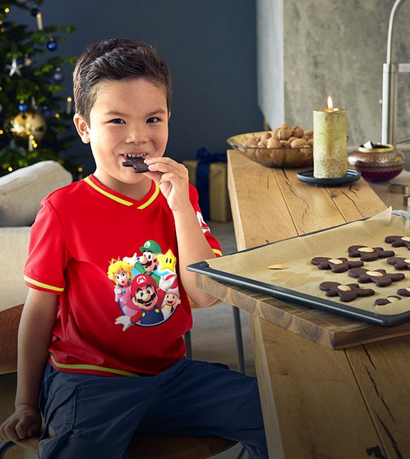 Jongen draagt kleding uit de Super Mario x Strauss-collectie zit daarbij aan een bar en eet koekjes